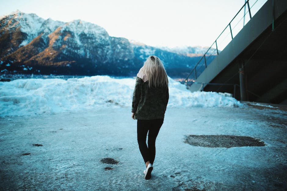 An image showing a person walking cautiously on an icy street, wearing slip-resistant boots and using a handrail for support.